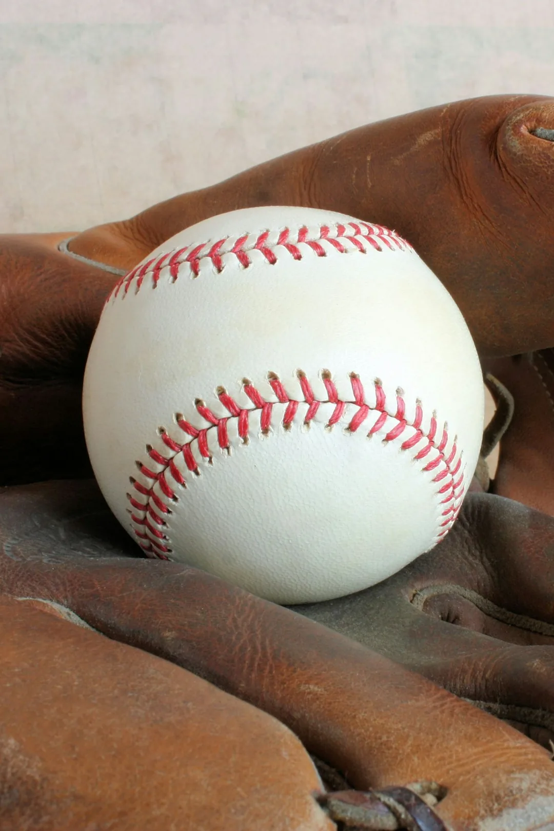 A baseball with red stitching resting in a worn leather glove