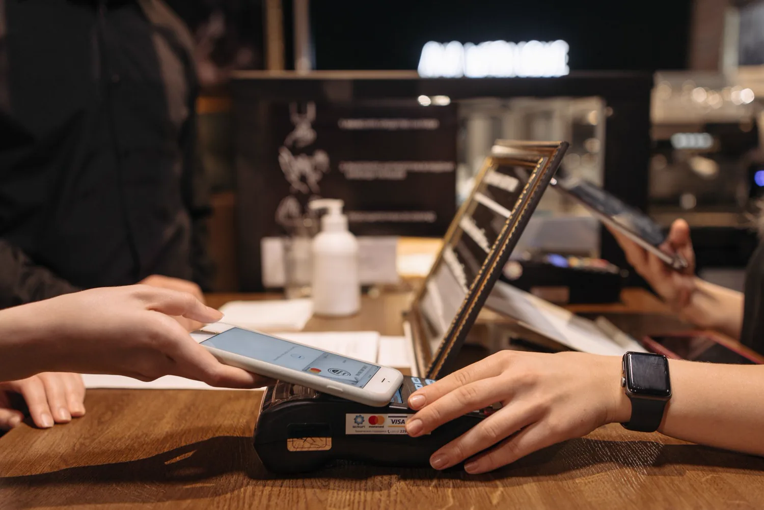 A shopper tapping a phone on a contactless payment terminal at checkout