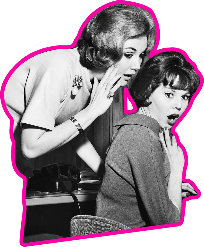 Two coworkers whispering at a desk